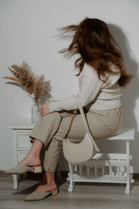 Full length of young woman sitting on table against wall at home