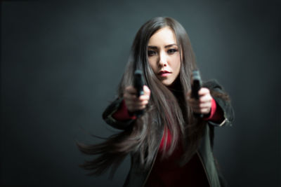 Portrait of young woman holding guns against black background