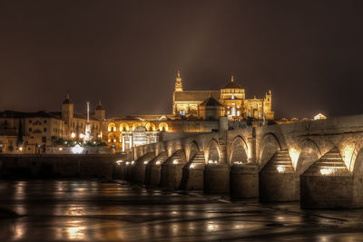 Illuminated bridge over river against buildings