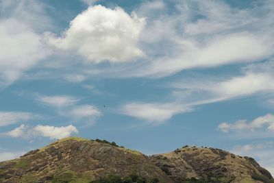 Small mountain against blue sky with clouds