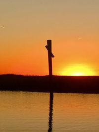 Silhouette pole by sea against dramatic sky during sunset