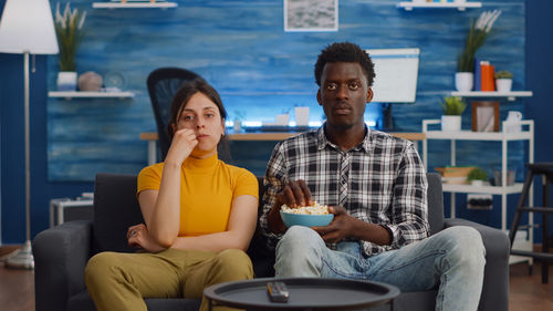 Portrait of couple eating popcorn while watching movie at home