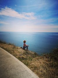 Woman sitting on field against sea