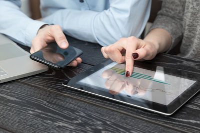 Midsection of colleagues using phones and digital tablet by laptop on desk