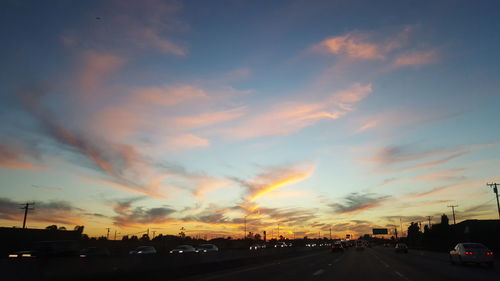 Vehicles on country road against dramatic sky during sunset