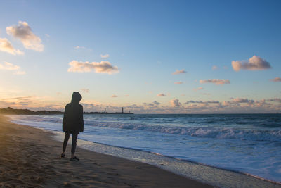 Rear view of teenager standing on beach during sunset