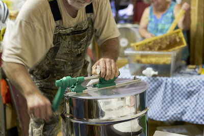 Midsection of man mixing honey in extractor indoors