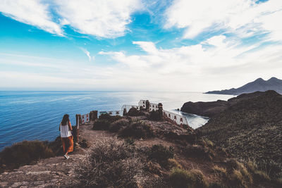 Rear view of woman walking on ridge against sea and sky