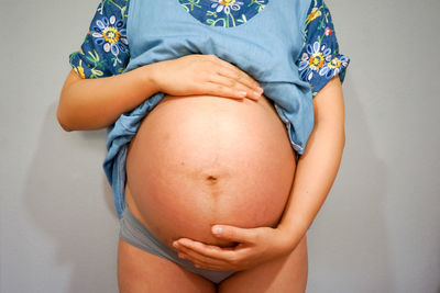 Midsection of pregnant woman in nightwear standing against wall