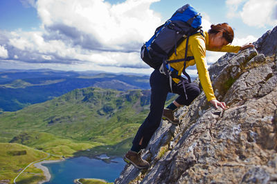 Woman with rucksack scrambling up snowdonia mountain