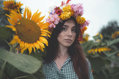Portrait of beautiful woman wearing floral wreath by sunflower at farm