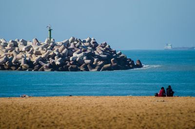 People on rocks by sea against clear sky