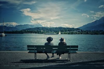 Rear view of couple sitting on lake against sky