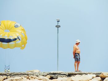 Rear view of man standing on rocks against clear sky