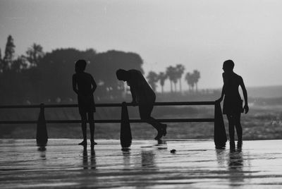 Silhouette people standing by swimming pool against sky