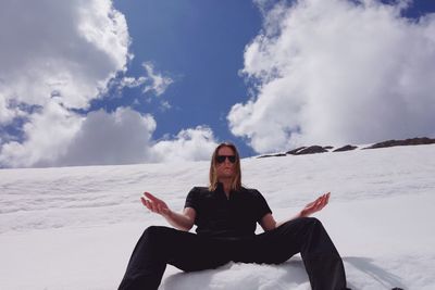 Low angle portrait of man sitting on snowcapped mountain against cloudy sky