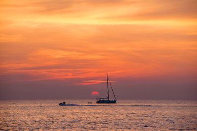 Sailboat sailing on sea against orange sky