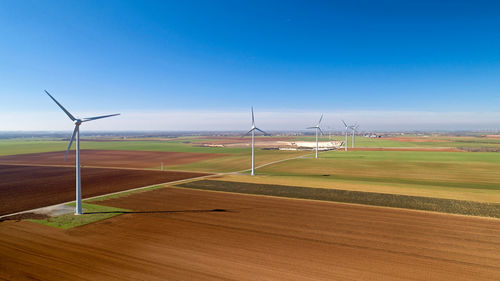 Aerial view of wind turbines on land against blue sky