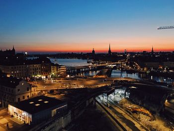 High angle view of illuminated city by river against sky during sunset