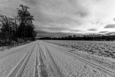 Tire tracks on agricultural field against sky during winter