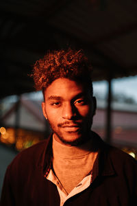 Young african american hipster male with curly hair and beard wearing warm jacket looking at camera while standing against shabby wall