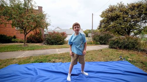 Full length portrait of smiling boy standing in park against sky