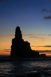 Silhouette rock formation on beach against sky during sunset