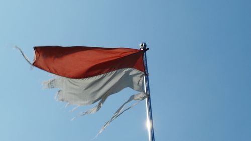 Low angle view of torn flag against clear blue sky