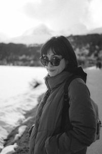 Portrait of young woman wearing sunglasses while standing against lake