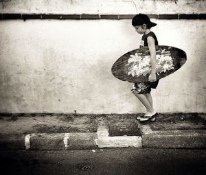 Full length of boy with surfboard walking on sidewalk against wall