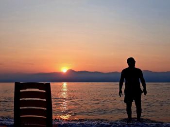 Rear view of silhouette man standing by sea against sky during sunset