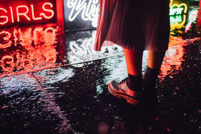 Low section of girl standing on wet footpath at night