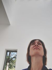 Low angle portrait of woman looking away against wall at home