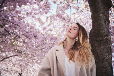 Young woman standing under cherry blossom