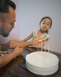 Father is lighting candles on birthday cake with little girl.