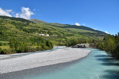 Scenic view of river by mountains against blue sky