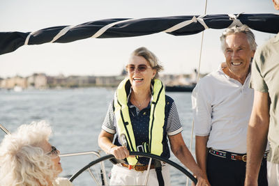 Cheerful senior woman sailing boat with happy friends on sunny day