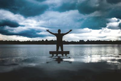 Silhouette person standing by lake against sky