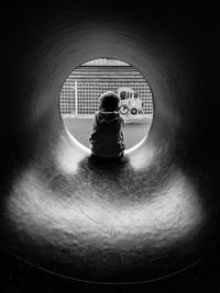 Rear view of boy sitting in pipe at playground