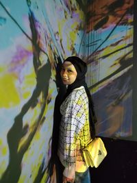 Portrait of young woman standing against wall