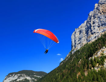 Low angle view of person paragliding by cliff against clear blue sky