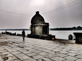 Rear view of people walking by mosque against sky