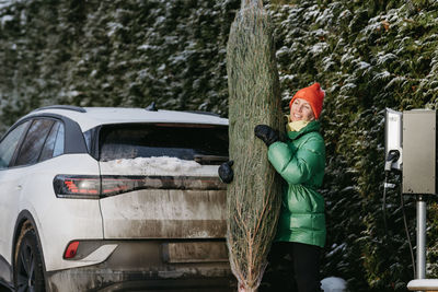 Smiling woman standing with christmas tree near car