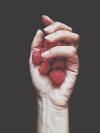 Cropped image of hand holding strawberry against black background