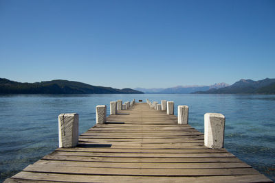 Pier over lake against clear blue sky