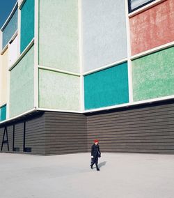 Rear view of man walking on footpath against building