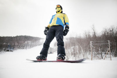 Low angle view of man standing on snowboard at field against sky
