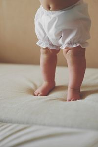 Low section of child standing on bed at home