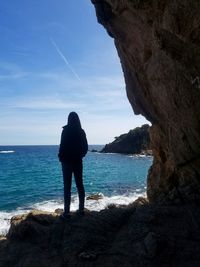 Rear view of woman standing on rock at beach