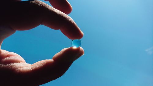 Close-up of hand holding crystal ball against sky